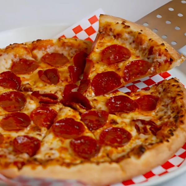 A slice of pepperoni pizza being lifted from a whole pizza on a white plate with red checkered paper.