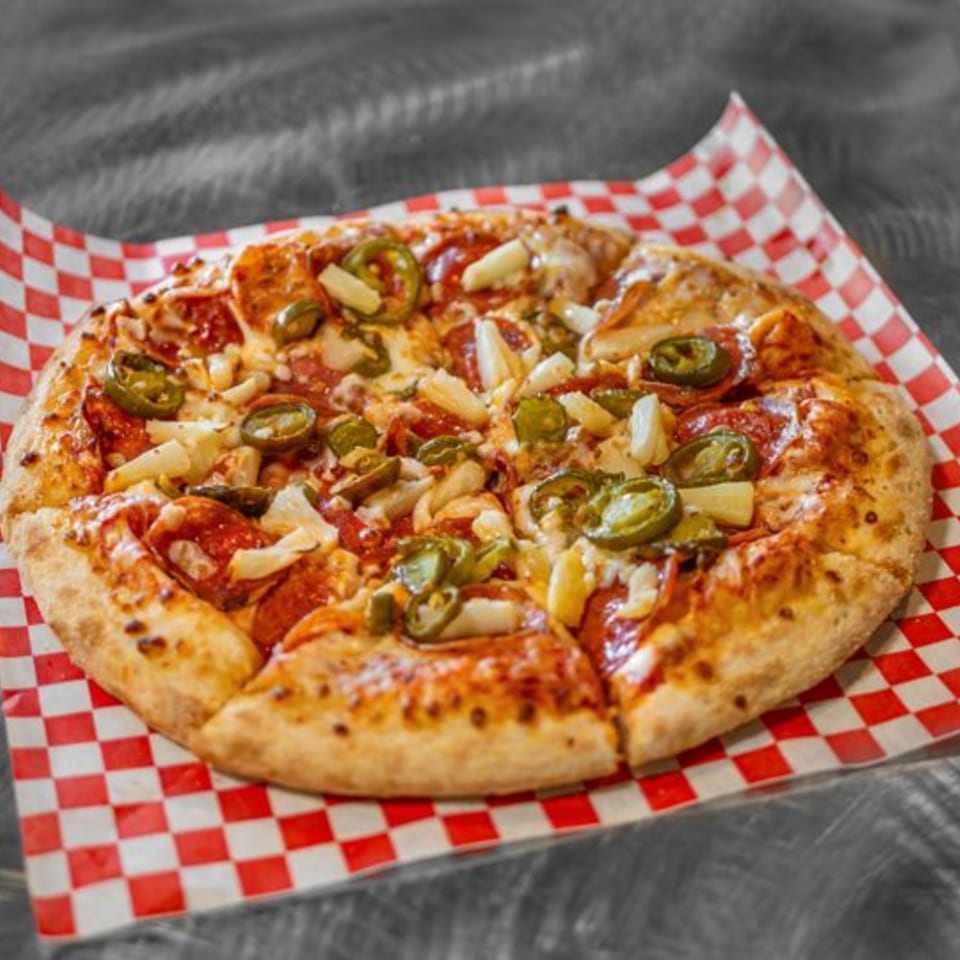 A Pizza Time Pub pizza with pepperoni, pineapple, and jalapeños on checkered paper.